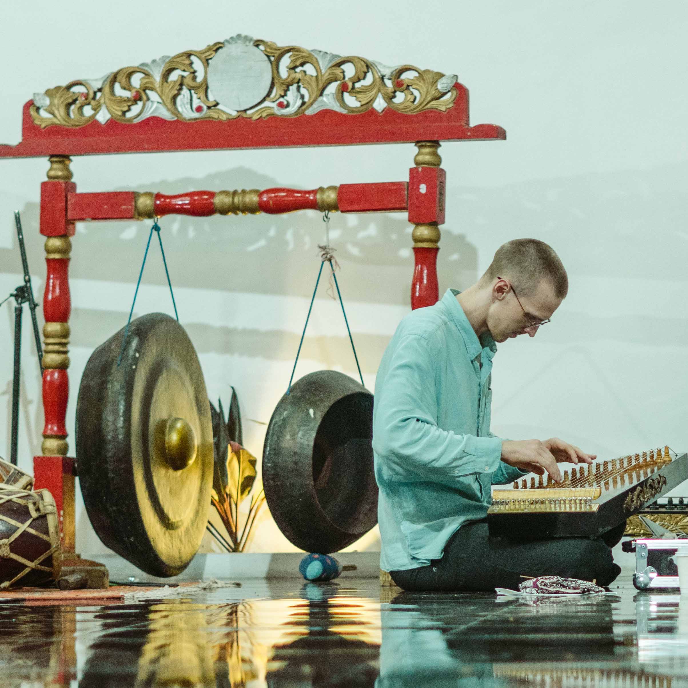 Kristofer playing kacapi with gongs in the background.