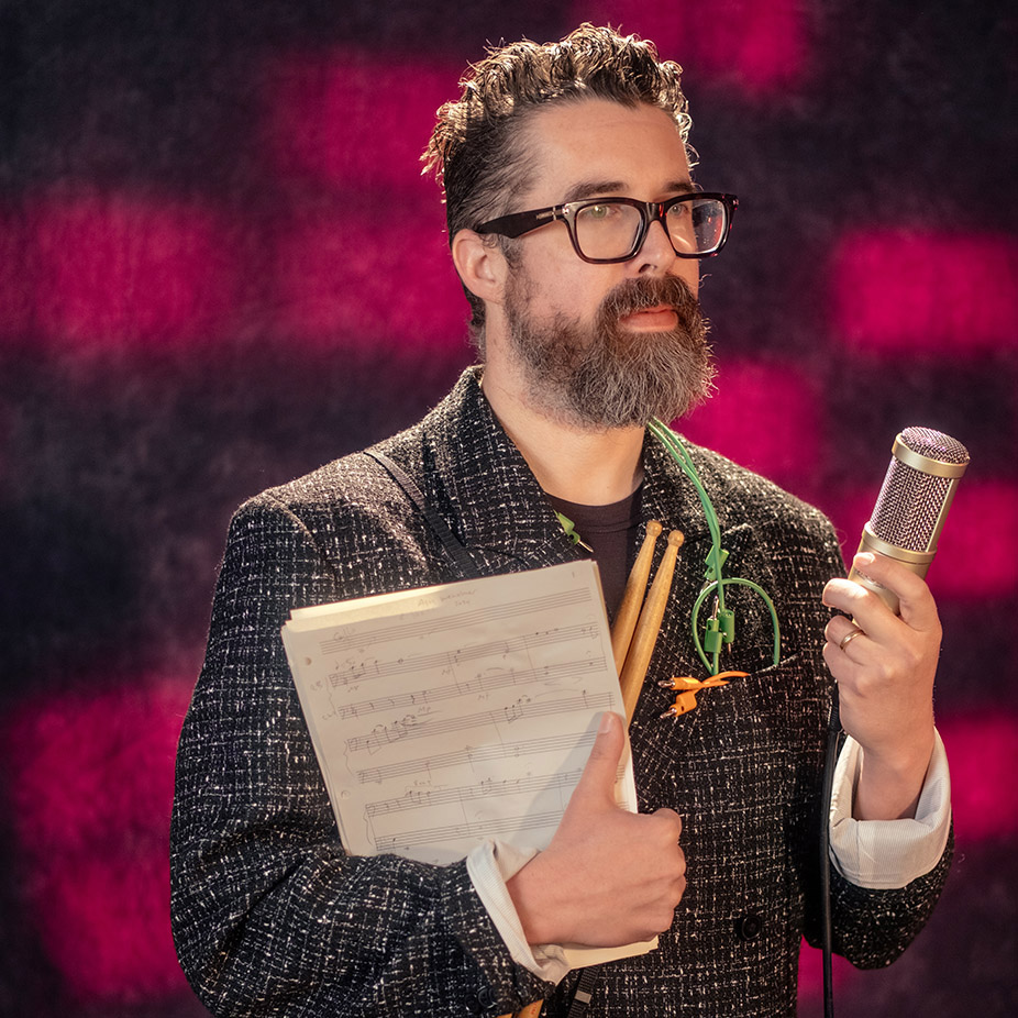Nat's glam shot in a suit with a camera and musical tools